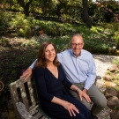 A man and women sit on a bench in a garden